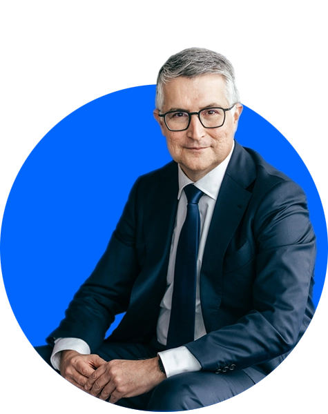 Santiago Argelich Hesse in Businesskleidung vor blau-weißem Hintergrund.