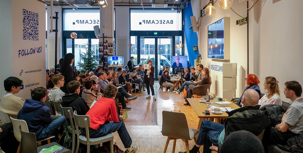 Gruppe von Menschen bei einem Vortrag; zwei Vortragende stehen vorne im Raum.