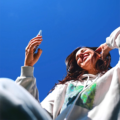 Frau in Sportkleidung schaut lächelnd auf ihr Handy bei sonnigem Wetter.