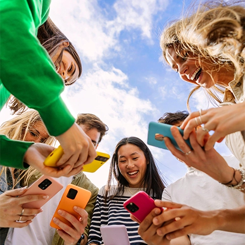 Sechs lächelnde Personen mit bunten Smartphones vor blauem Himmel mit Wolken.