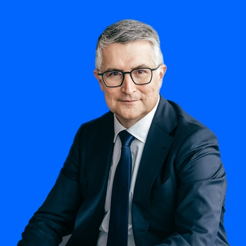 Santiago Argelich Hesse smiles in a dark suit in front of a blue background.