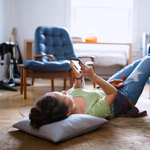 Woman lying relaxed on the living room floor looking at her cell phone.