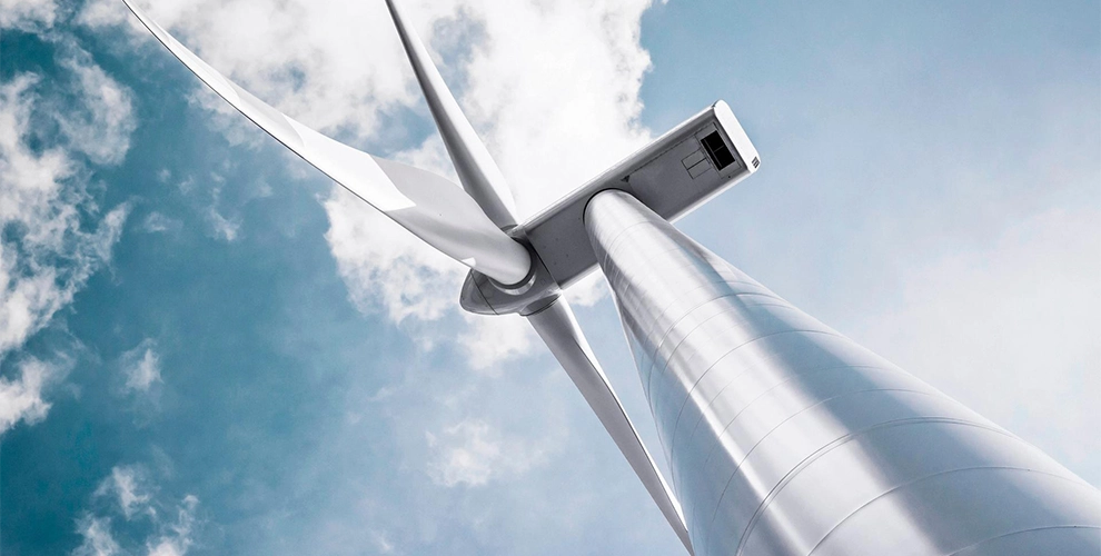Wind turbine seen from below against a light blue sky with clouds.