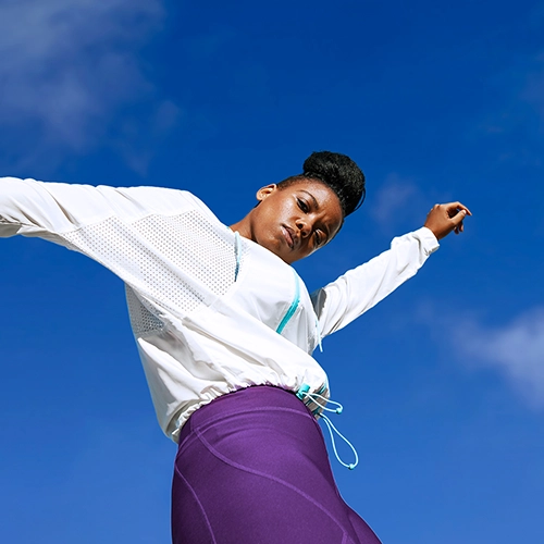 Woman in sportswear moving her arms against a blue sky with clouds.
