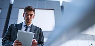Man in a suit reading documents in front of a gray building with windows.