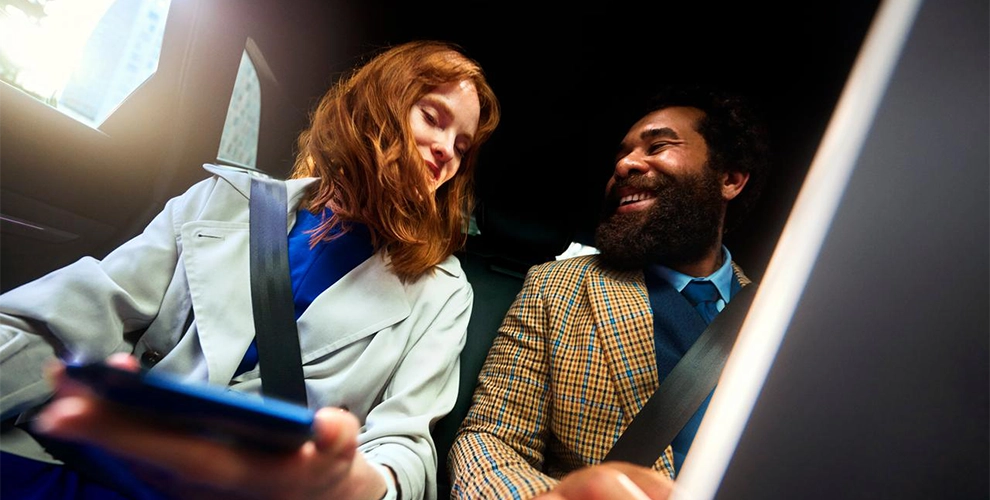 Man and woman sitting in a car, each holding a smartphone.